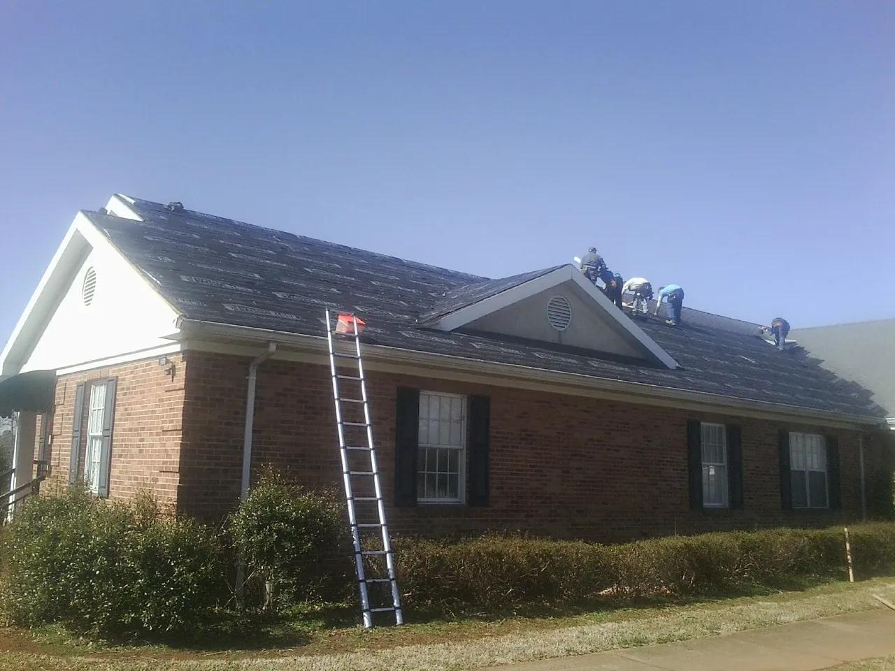 Crew tearing shingles off a brick ranch roof with a ladder set — Emergency Roof Repair work by our crew in Lynchburg