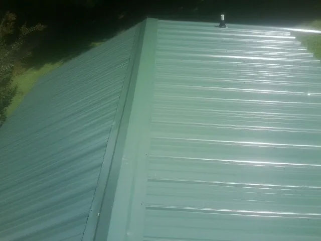 New green metal panels meeting at the ridge of a roof — Flat Roof Repair work by our crew in Lynchburg