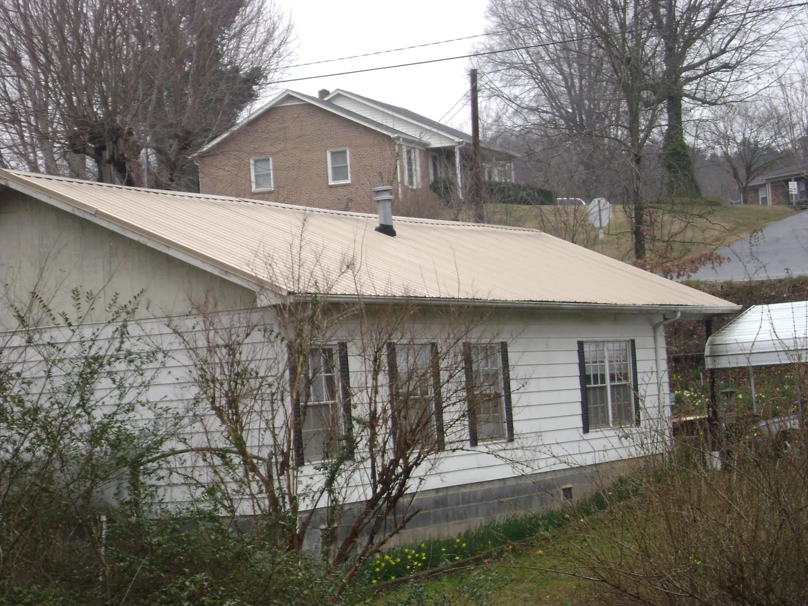 Tan metal roof on a white sided house set into a hillside — Commercial Roofing by Roofing Brothers in Lynchburg